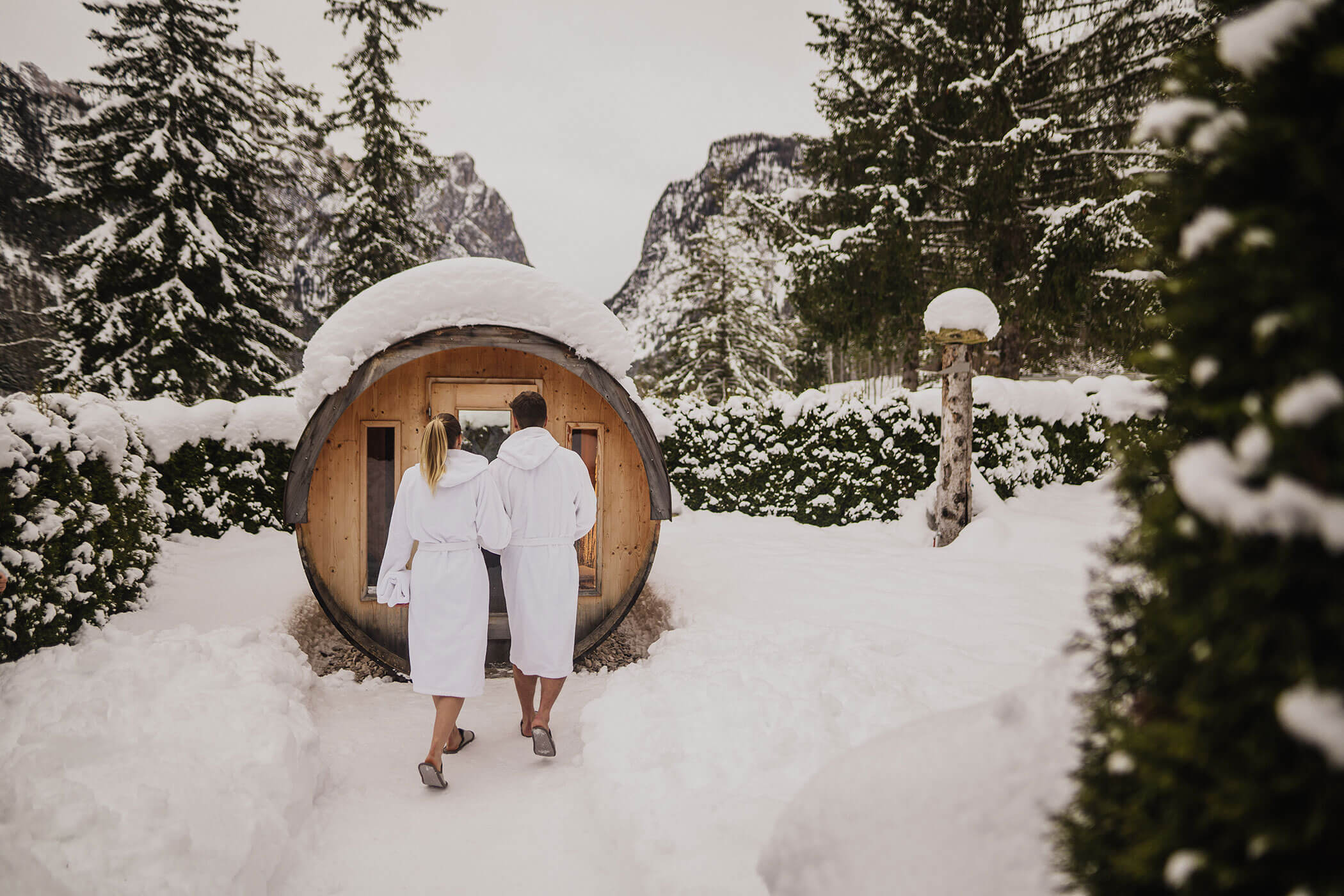 Ein Paar auf dem Weg in die verschneite Außensauna im Winter - Camping Toblacher See
